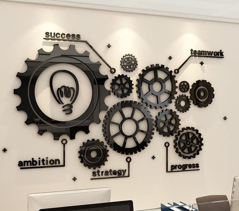 אמנות הקיר מציגה גלגלי שיניים שחורים משולבים עם סמל נורה ומילים: הצלחה, שאפתנות, אסטרטגיה, עבודת צוות והתקדמות הקשורות לגלגלי שיניים שונים.